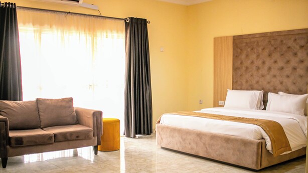 Habitación de hotel con cama, sofá, una pequeña mesa redonda y ventana con cortinas.