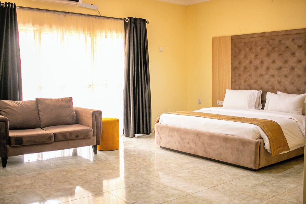 Habitación de hotel con cama, sofá, una pequeña mesa redonda y ventana con cortinas.