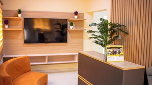 Un área de recepción moderna con un televisor de pantalla plana, un mostrador de madera, un sofá y una planta en maceta.