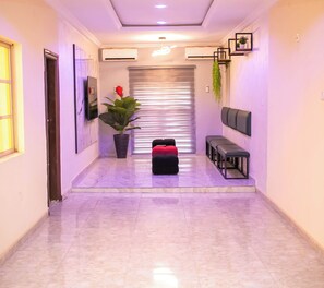 A hallway with a marble floor, a potted plant, a bench, and a wall-mounted TV. - Cedar Suites (Ibadan)