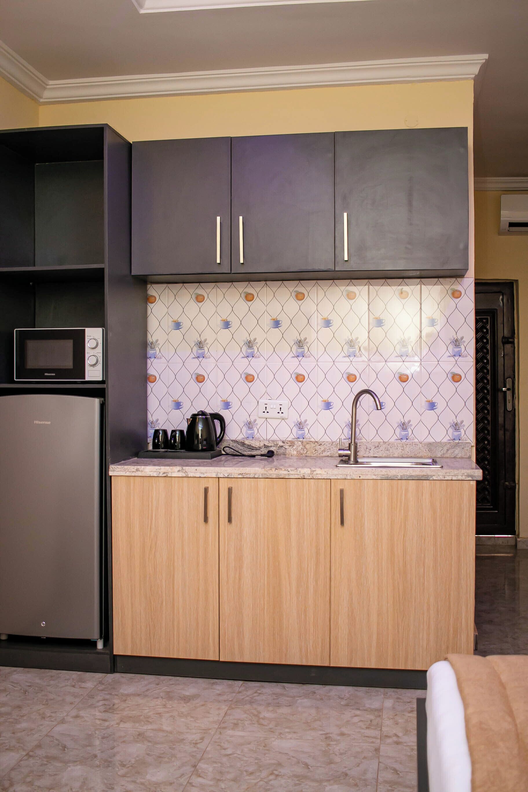 Una cocina compacta con microondas, hervidor y pileta.
