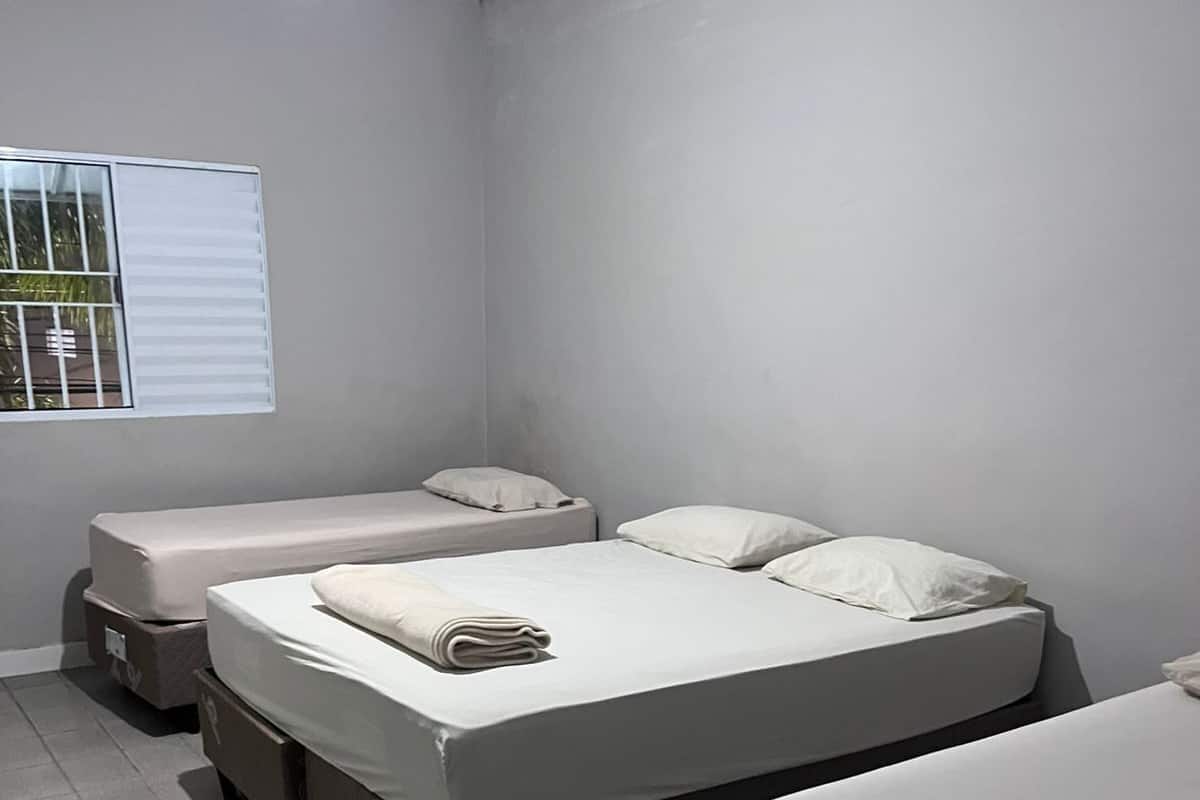 Una habitación con tres camas, una ventana con persianas y un ventilador de techo.