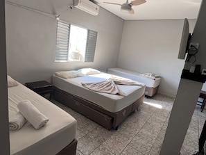 A hotel room with a bed, a bedside table, a desk, a chair, a window, and an air conditioning unit. - Pousada Aviação (Praia Grande)