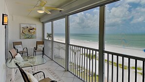 Un balcone con un tavolo e sedie in vetro, una ventola a soffitto e vista sulla spiaggia.