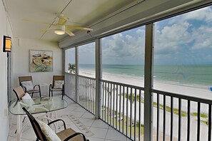Ein Balkon mit Glastisch und Stühlen, einem Deckenventilator und Blick auf den Strand.