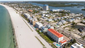 Vista aerea di una località costiera con spiaggia, un porto turistico e diversi edifici, tra cui hotel.