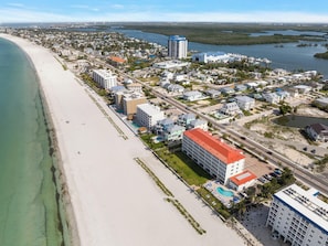 Luftaufnahme einer Küstenstadt mit Strand, einer Marina und verschiedenen Gebäuden, darunter Hotels.
