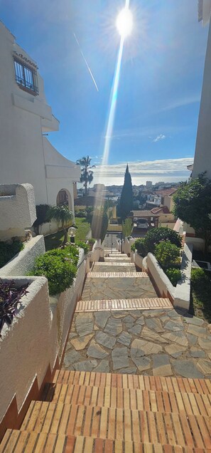 A pathway leading to a building with a view of the sea, stone steps, and greenery. - Cozy One-Bedroom Apartment with Terrace and Sea Views (Mijas-Costa)