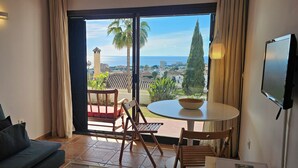 Et værelse med balkon, en sofa, et bord med en skål og et fjernsyn ophængt på væggen.