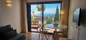 A room with a balcony, a sofa, a table with a bowl, and a TV mounted on the wall. - Cozy One-Bedroom Apartment with Terrace and Sea Views (Mijas-Costa)