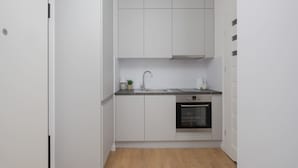 Eine kompakte Küche mit weißen Schränken, einer Edelstahl-Spüle und einem Backofen.
