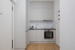 Eine kompakte Küche mit weißen Schränken, einer Edelstahl-Spüle und einem Backofen.