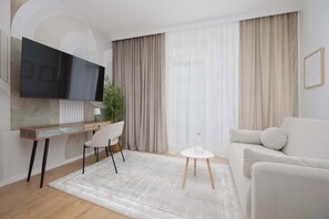 Ein modernes Wohnzimmer mit Flachbildfernseher, Schreibtisch mit Stuhl, Sofa und Couchtisch.