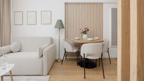 Ein modernes Wohnzimmer mit einer Couch, einem runden Esstisch mit Stühlen, einer Stehlampe und gerahmten Kunstwerken an der Wand.
