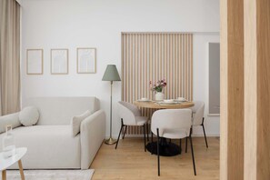 Ein modernes Wohnzimmer mit einer Couch, einem runden Esstisch mit Stühlen, einer Stehlampe und gerahmten Kunstwerken an der Wand.