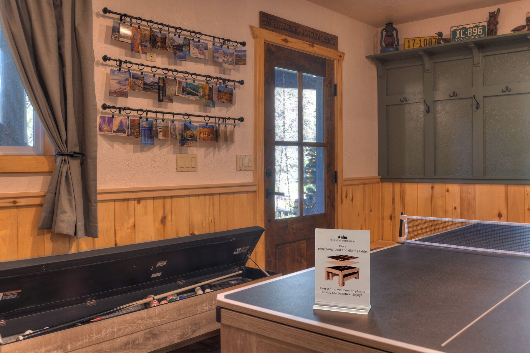 Una habitación con mesa de billar, un atril de pared con fotografías de viajes, una puerta con vistas y un armario con un cartel.