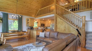 Ein großzügiges Wohnzimmer mit Ledersofa, einem Esstisch und einer Küchenzeile mit Holzausbau und einer Treppe.