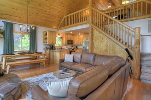 Ein großzügiges Wohnzimmer mit Ledersofa, einem Esstisch und einer Küchenzeile mit Holzausbau und einer Treppe.