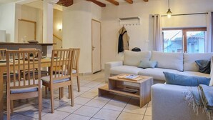 Ein Wohnzimmer mit einer Couch, Sesseln, einem Couchtisch und einem Essbereich mit Tisch und Stühlen.