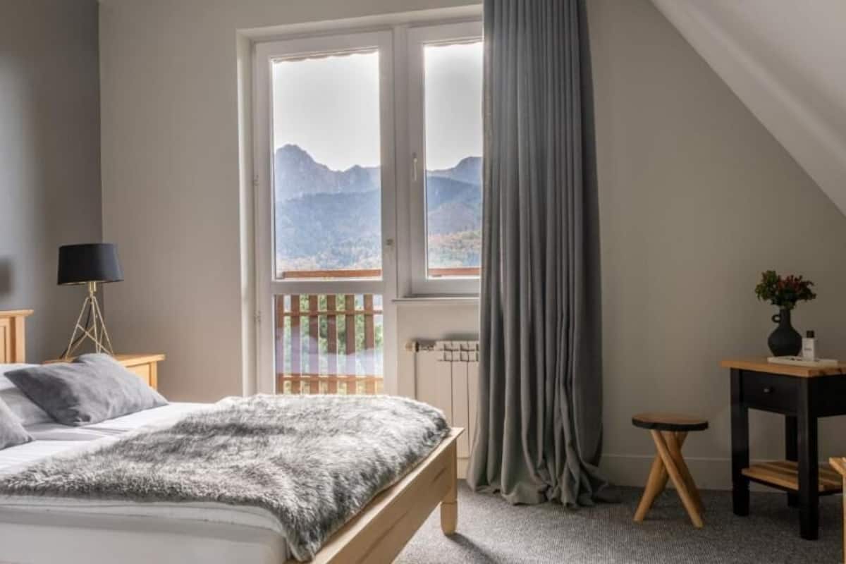 Un dormitorio con cama, una ventana con vistas, una lámpara y una mesita.