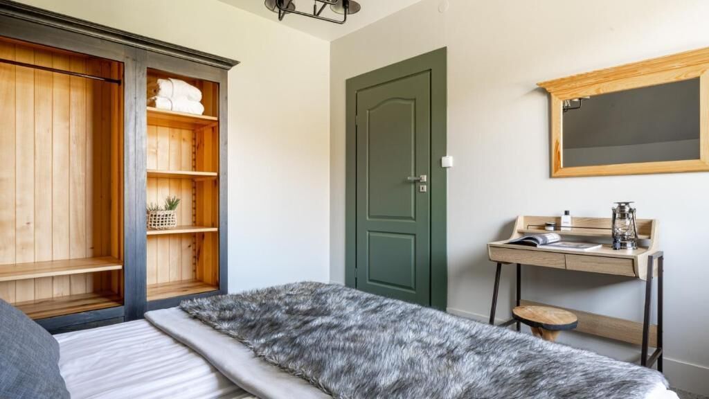 A bedroom with a bed, a desk with a chair, a green door, and a wardrobe.