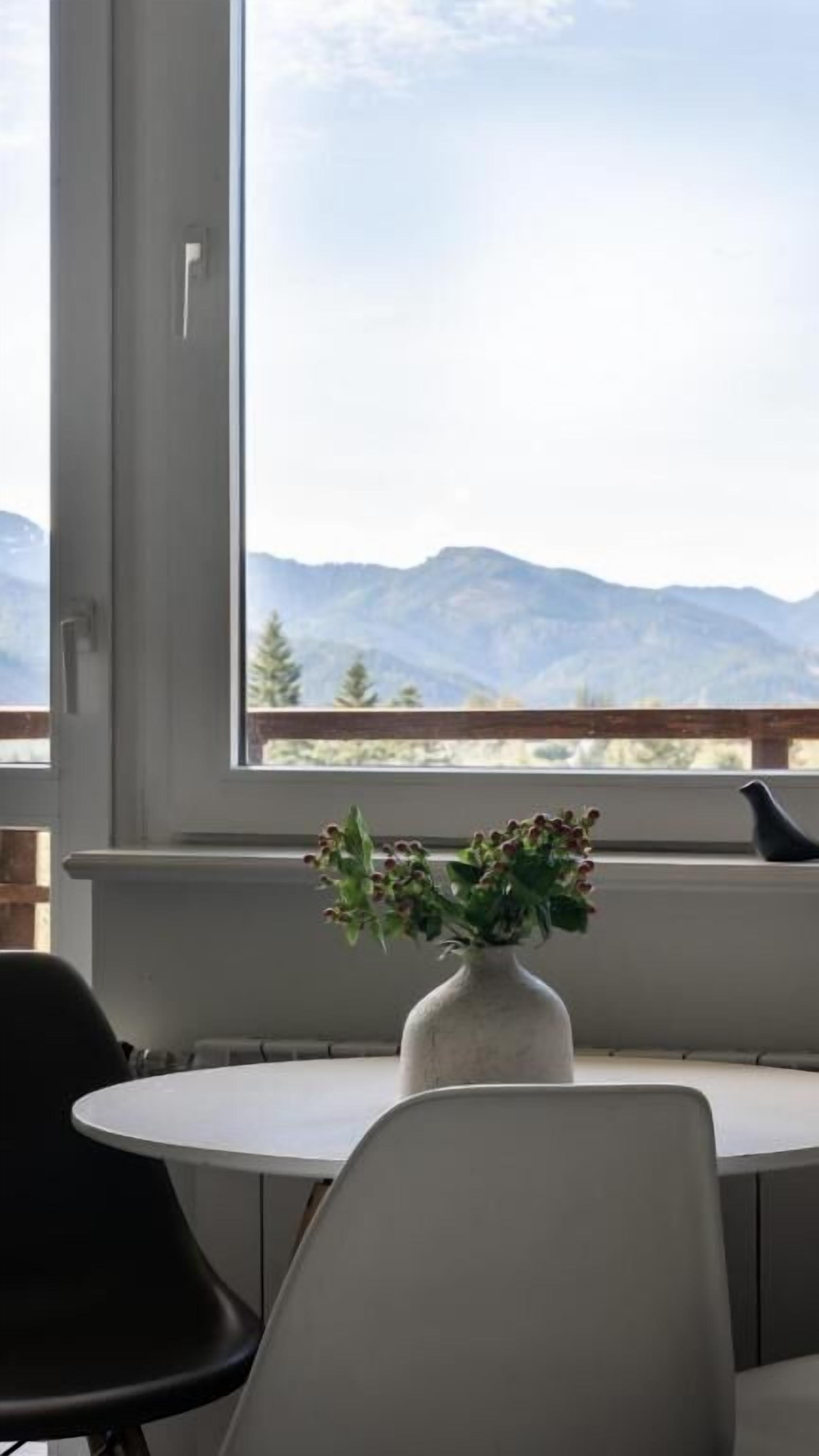 Ein Zimmer mit einem großen Fenster, einem runden Tisch und einer Vase mit Blumen.