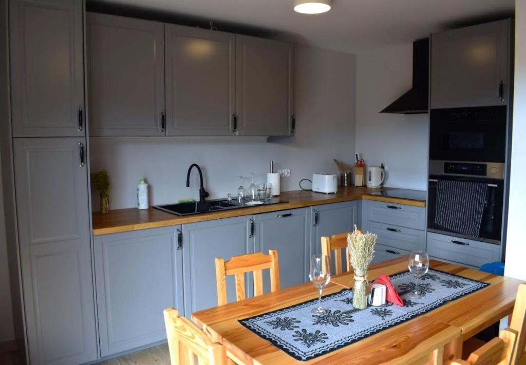 A kitchen with grey cabinets, a wooden countertop, a dining table with a placemat, and a built-in oven.