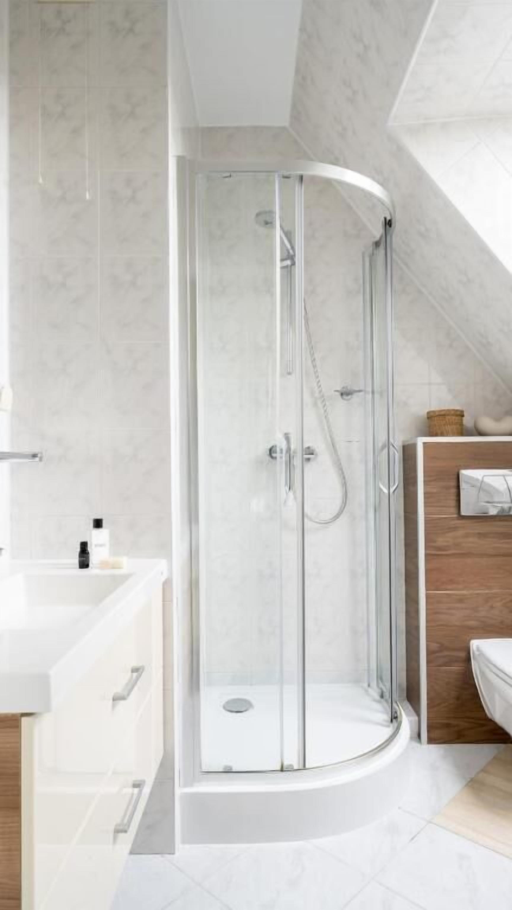A modern shower enclosure with a glass door, a wooden vanity with a mirror, and a white countertop.