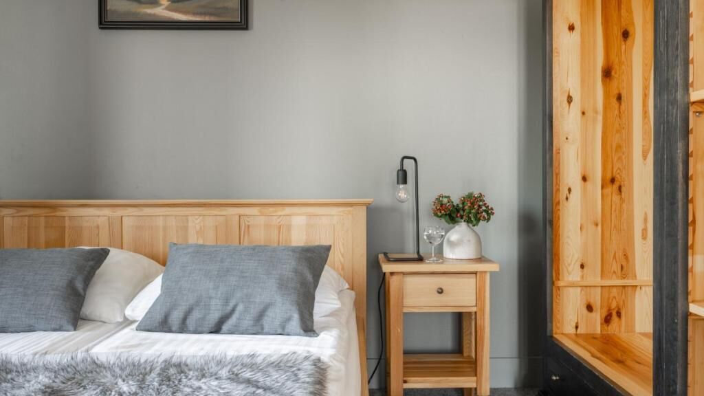 Une chambre à coucher avec une tête de lit en bois, une petite table de chevet avec une lampe et une fenêtre dotée de volets en bois.