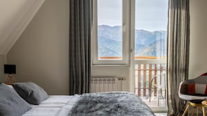 Un dormitorio con cama, ventana, radiador y balcón con vistas a montañas.