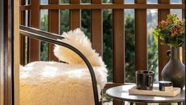 Un balcone con vista sulle montagne, una sedia, un tavolino con un vaso e una tazza.
