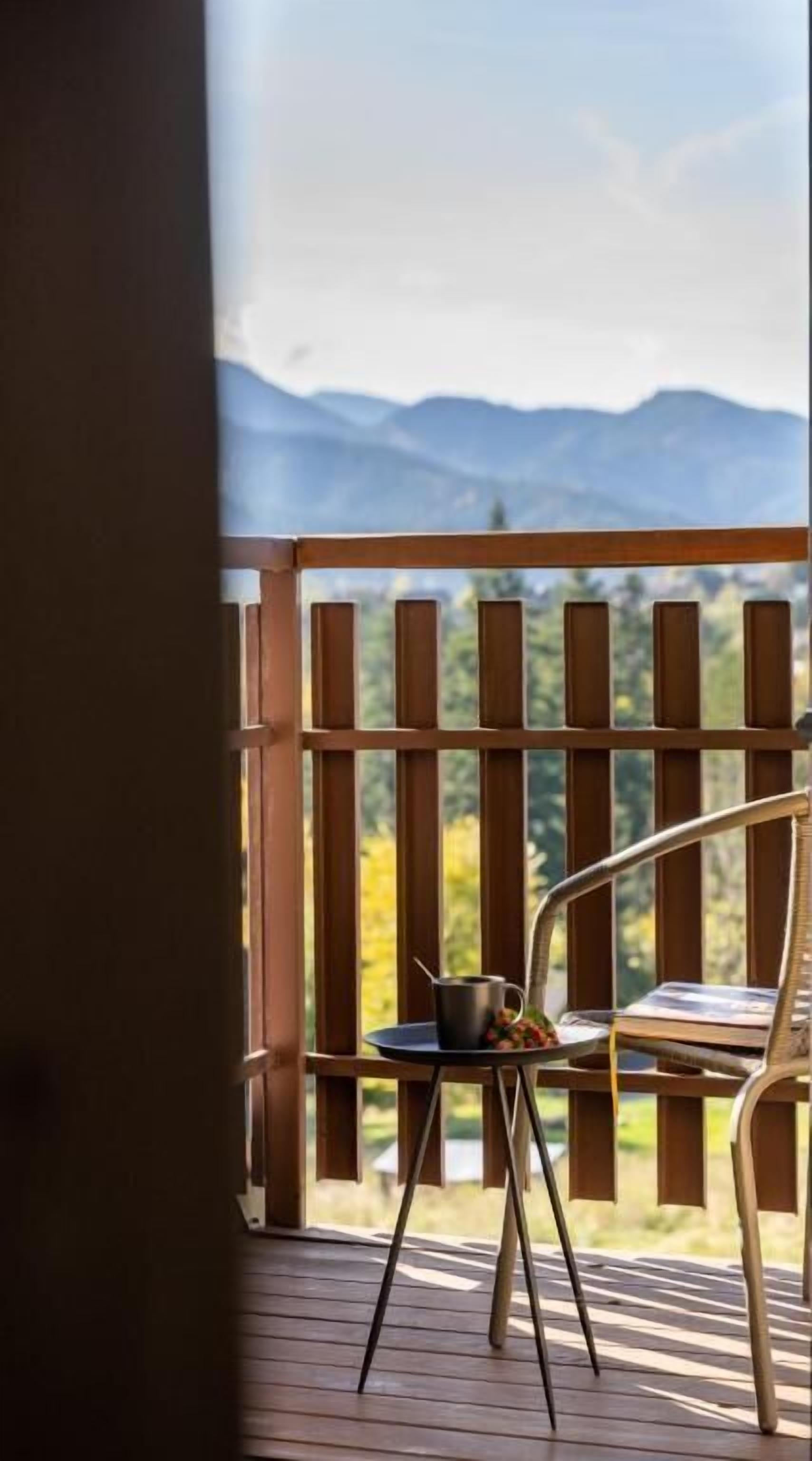Una terraza de madera con una silla y una mesa, vista a las montañas y cielo despejado.