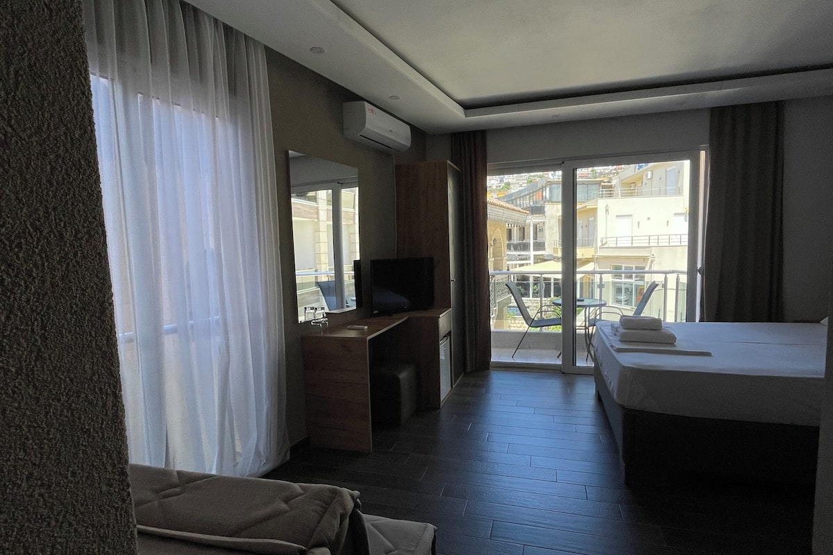 Habitación de hotel con cama, escritorio, televisión y balcón con vistas a edificios.
