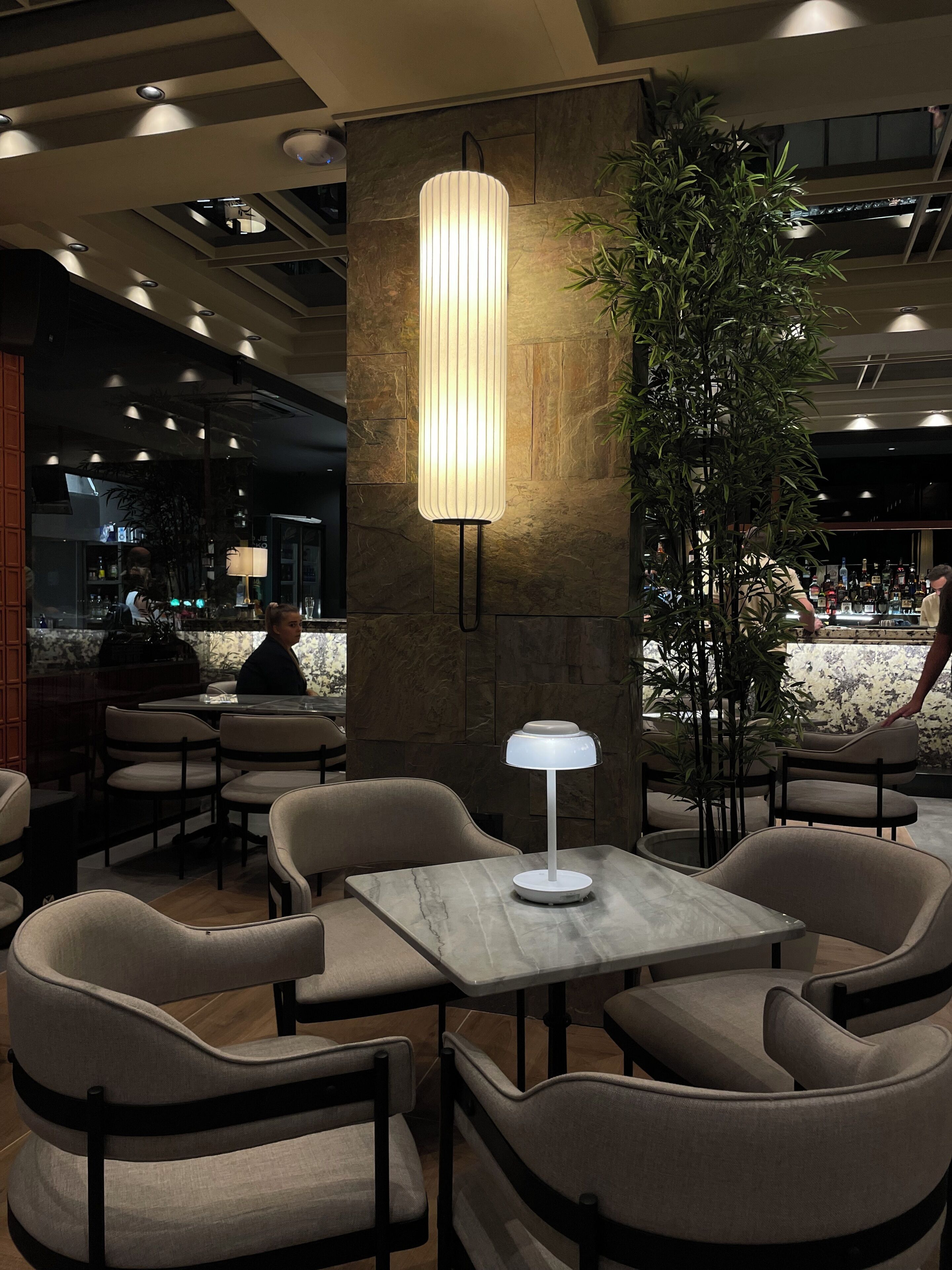 Un interior moderno con una zona de bar, asientos con mesas y una columna decorativa.