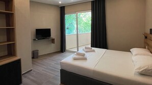 A modern hotel room with a large bed, a TV, a wooden shelf, and a balcony with a view. - Vue Mer Hotel (Ulcinj)