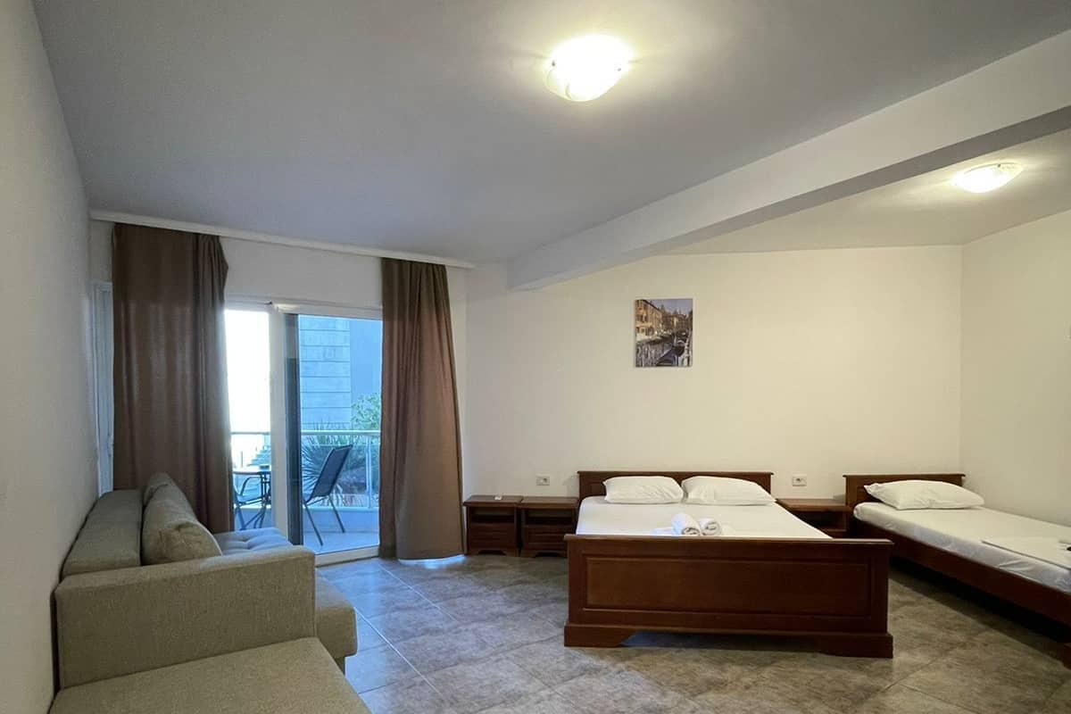Una habitación con cama, sofá, una mesita y ventana con cortinas.