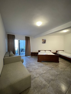 Una habitación con cama, sofá, una mesita y ventana con cortinas.