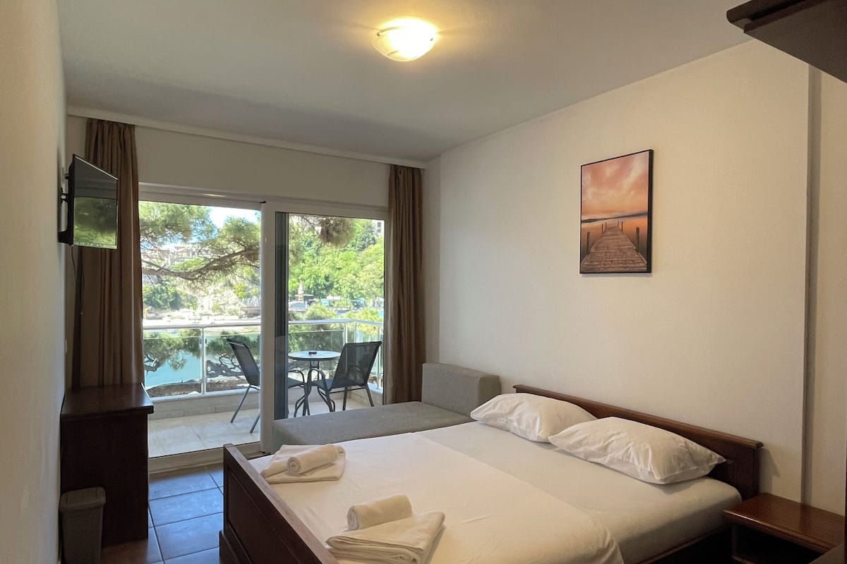 Habitación de hotel con cama, escritorio, silla y balcón con vistas.