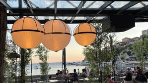 An outdoor dining area with tables and chairs, large hanging lamps, and a view of the sea and boats. - Vue Mer Hotel (Ulcinj)