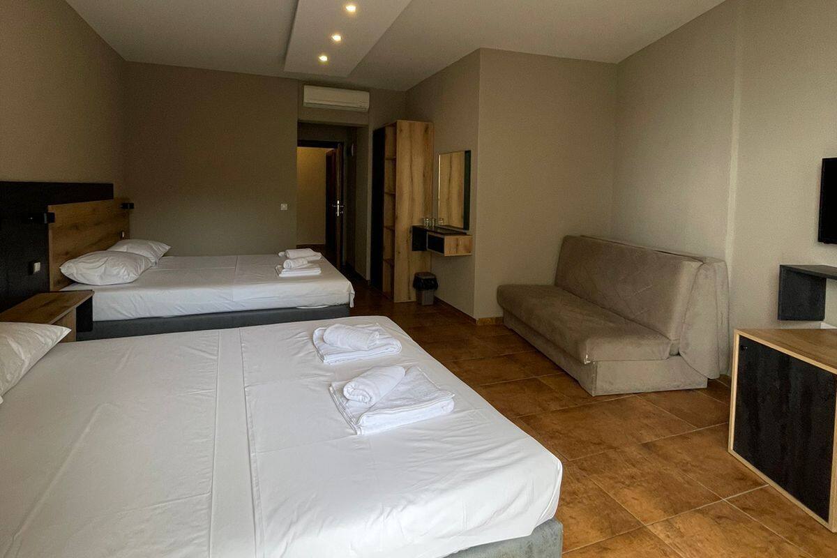 Habitación de hotel con dos camas, un sofá, un televisor y un mueble bajo.