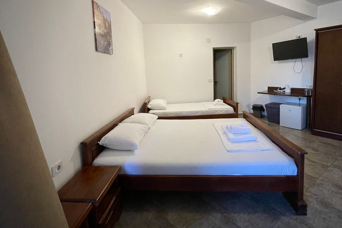 Habitación de hotel con dos camas individuales, un escritorio con silla, televisión y un refrigerador pequeño.