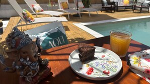 Une table placée au bord de la piscine, avec une part de gâteau, un verre de jus d’orange et une statuette d’éléphant décorative.