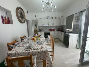 A modern kitchen with white cabinets, a dining table set with floral tablecloths, and a clock on the wall. - Holiday Home 'Ar Doce' with Private Pool, Wi-Fi and Air Conditioning (Portel)