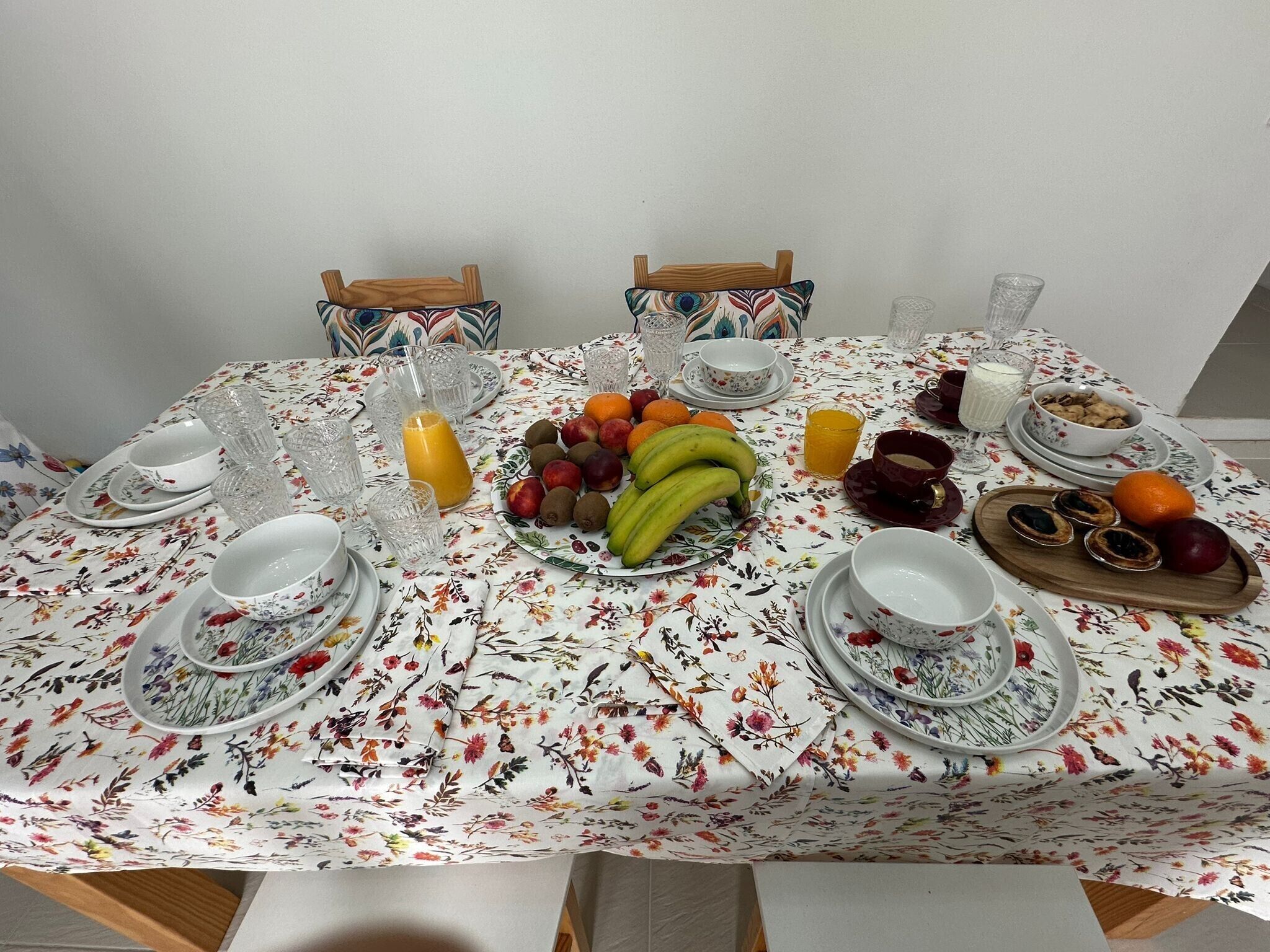 Una mesa de comedor servida con platos, vasos y una variedad de frutas y pasteles.
