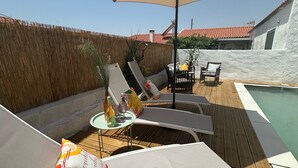 Un espace aménagé au bord de la piscine, avec des chaises longues, une table avec des boissons et un grand parasol.