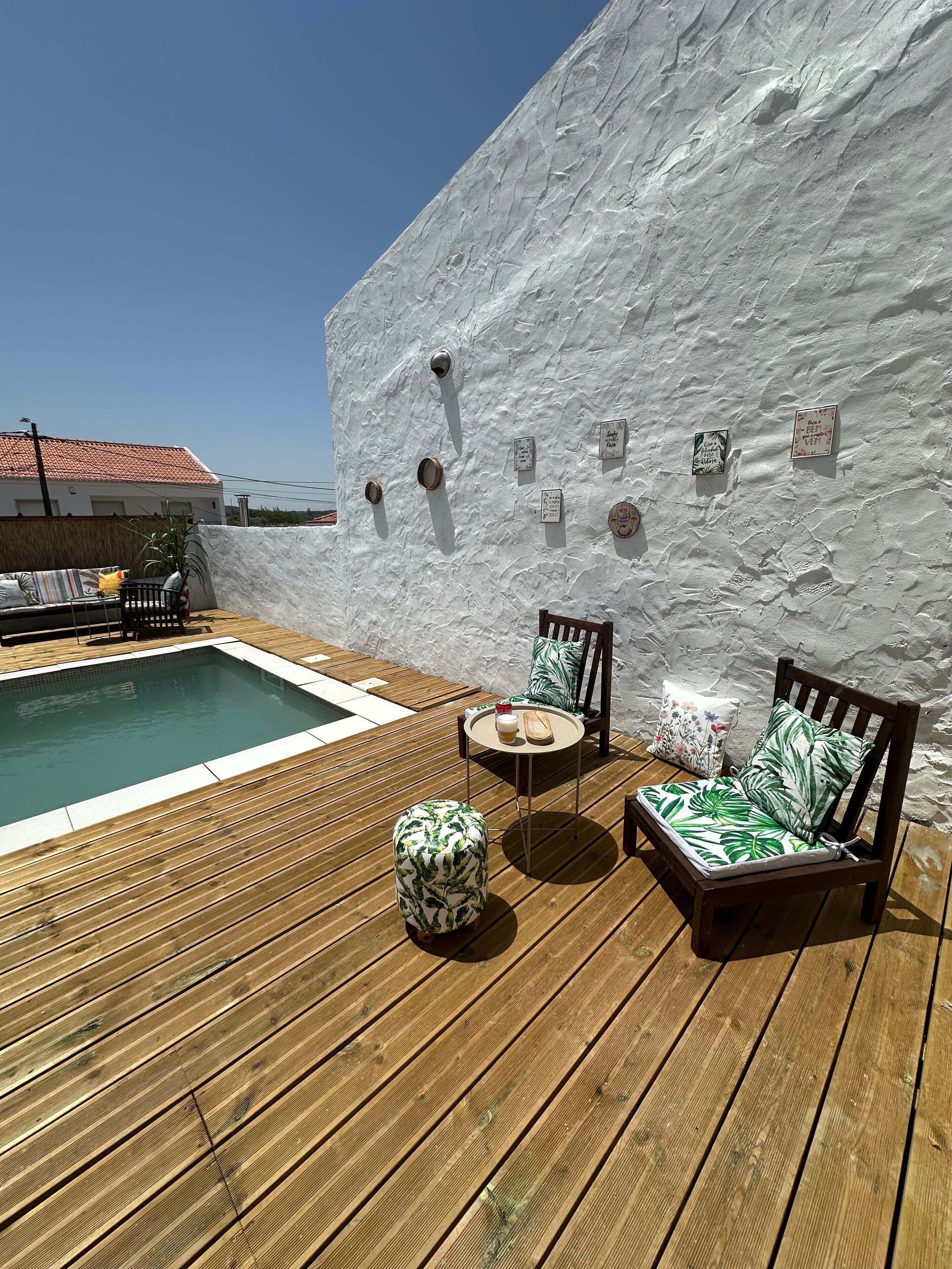 Une terrasse en bois avec une piscine, deux chaises, une petite table et un mur décoratif orné de panneaux.