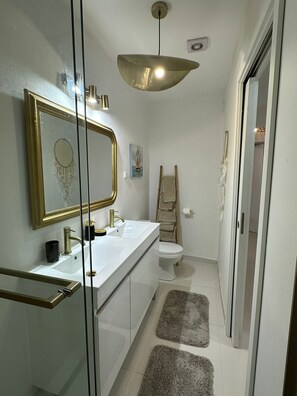 A modern bathroom with a glass shower enclosure, a white sink with gold fixtures, a toilet, and a towel rack. - Holiday Home 'Ar Doce' with Private Pool, Wi-Fi and Air Conditioning (Portel)