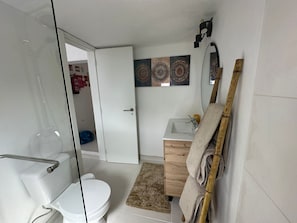 A bathroom with a toilet, sink, glass shower enclosure, wooden cabinet, decorative wall art, and a towel rack.
