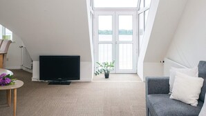 A modern living room with a television, a sofa, and a window with a view of a body of water. - 4 Person Holiday Home in Hejls (Hejls)