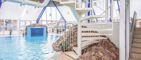 An indoor swimming pool with a stone wall and a white staircase leading to a roofed area.